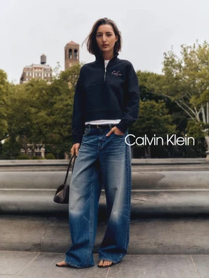 Model Haena Rumpf standing outdoors in wide-leg denim jeans and a dark zip sweatshirt holding a handbag.