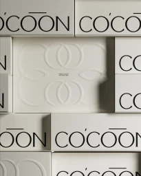 Grid of off-white Cocoon packaging boxes featuring embossed interlocking loop patterns and black typography.