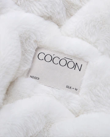 Close-up of a woven Cocoon brand label stitched onto soft white plush faux fur fabric.