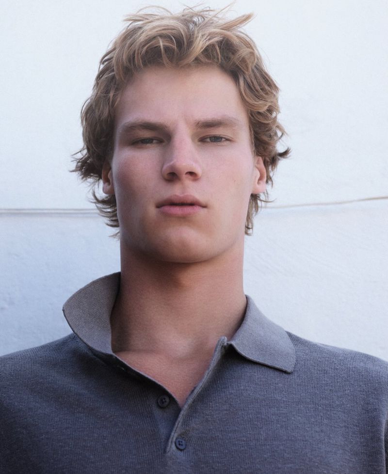 Portrait of a blond adult male wearing a grey collared shirt against a white background. Blond hair, neutral expression, fashion shot.