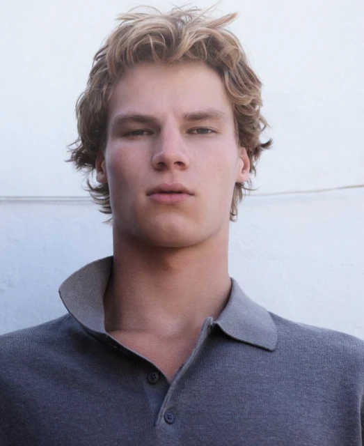 Portrait of a blond adult male wearing a grey collared shirt against a white background. Blond hair, neutral expression, fashion shot.