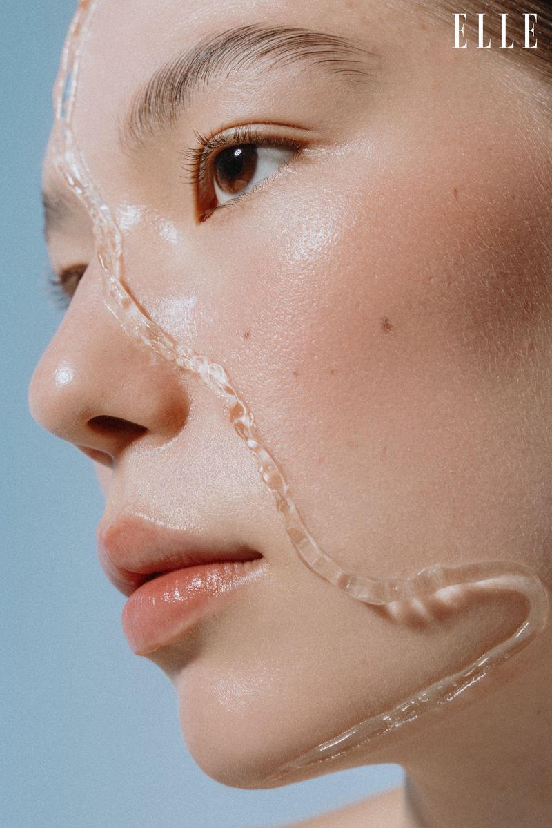 Close-up profile of a woman with a clear viscous liquid trail running across her cheek and chin, set against a solid blue background.