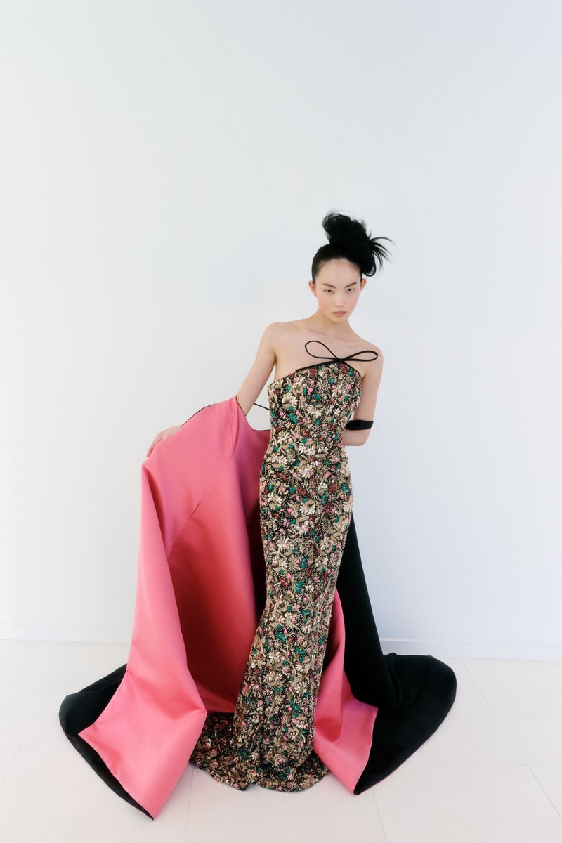 East Asian model wearing a floral print strapless gown with a large pink and black train against a white background.