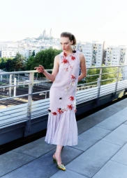 Model Fran Summers poses on a sunny rooftop terrace overlooking a cityscape wearing an embellished pale lilac drop-waist dress.