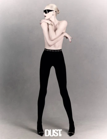Alex Consani wears black leggings, pointed heels, and wraparound sunglasses against a soft, neutral grey studio background.