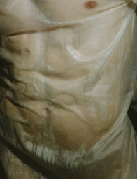 Close-up of a man's muscular torso and abdomen covered in clinging, wet translucent plastic wrap.