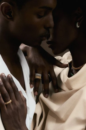 Close-up of a man and woman embracing while wearing textured gold and silver rings and fine jewelry in soft warm light.