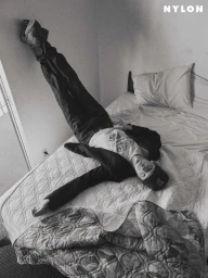 Monochrome high-angle shot of Role Model lying across an unmade bed with legs resting up against the wall in a jacket and jeans.
