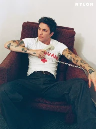 Role Model in a white lifeguard t-shirt and jeans sits in a burgundy armchair holding a corded phone receiver.