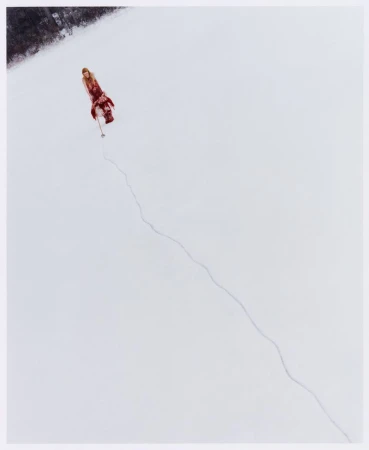 High angle shot of a woman in a long red patterned dress walking across an expansive snowfield leaving a trail in the snow.