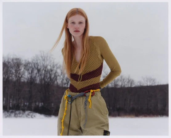 Model Lainey Hearn in knitwear and khaki pants posing outdoors against a snowy landscape and bare trees.