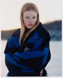 Model Lainey Hearn wearing an oversized blue and black winter sports jacket outdoors in a snowy landscape.
