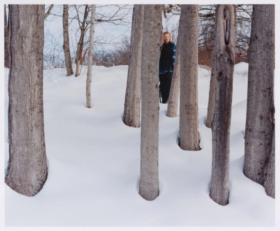 Model Lainey Hearn stands framed between bare tree trunks in deep winter snow for HARD PACK Magazine.