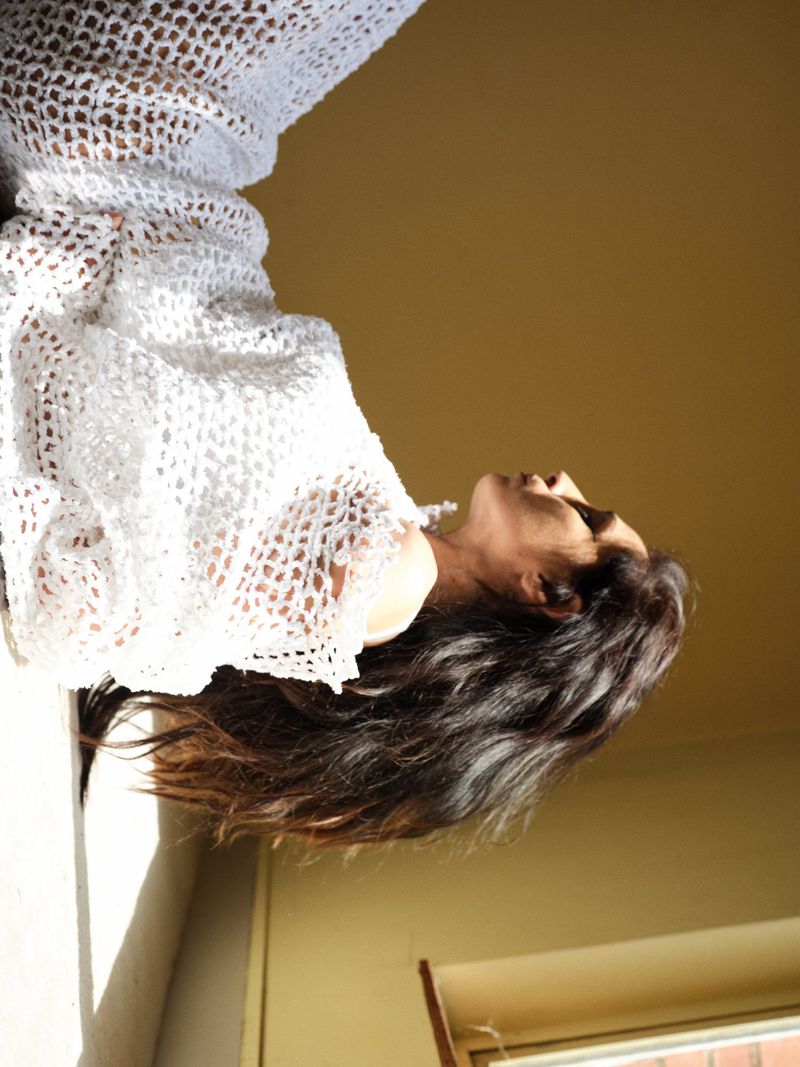 Yasmine Hamdan in profile wearing a white open-knit crochet top under warm directional sunlight.