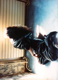 Yasmine Hamdan sitting on the floor in a black leather jumpsuit leaning against a panelled wall.