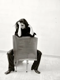 Yasmine Hamdan seated backwards on a modern chair leaning on her hand in all-black attire against a plain studio wall.