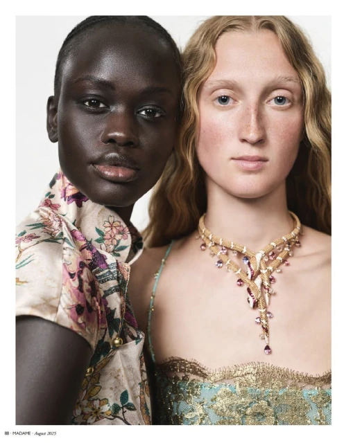 Close-up portrait of two women in a photo studio. The blonde woman wears a gold and jewel necklace and gown. The other model wears a floral top.
