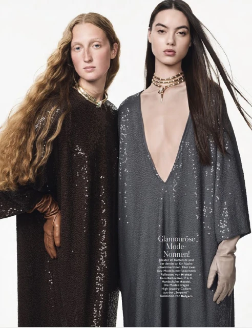 Two fashion models pose in sequined dresses and gloves against a stark white background, accessorized with gold chokers, for a studio editorial.