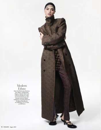 Model wearing an oversized brown patterned high-neck coat and split-hem trousers against a white seamless background.