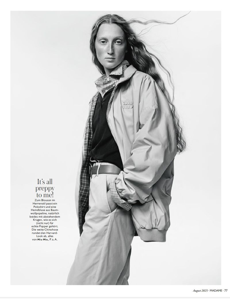 Black and white fashion portrait of a model wearing an oversized blouson jacket, polo shirt, and belted chinos on a white backdrop.