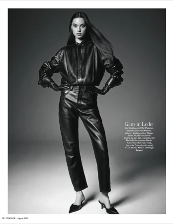 Monochrome fashion shot of a slender woman in a black leather outfit with mules, captured in a full shot against a plain gray backdrop.