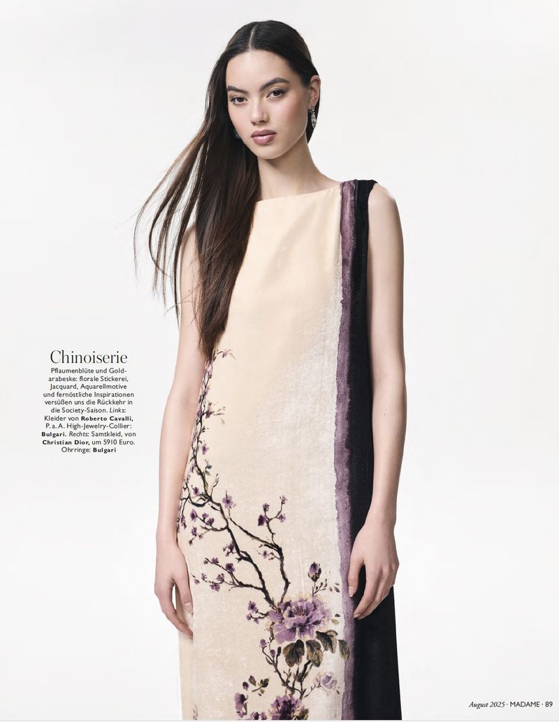 Model in a sleeveless cream chinoiserie dress with purple floral illustration against a plain white studio background.