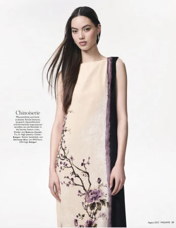 Model in a sleeveless cream chinoiserie dress with purple floral illustration against a plain white studio background.