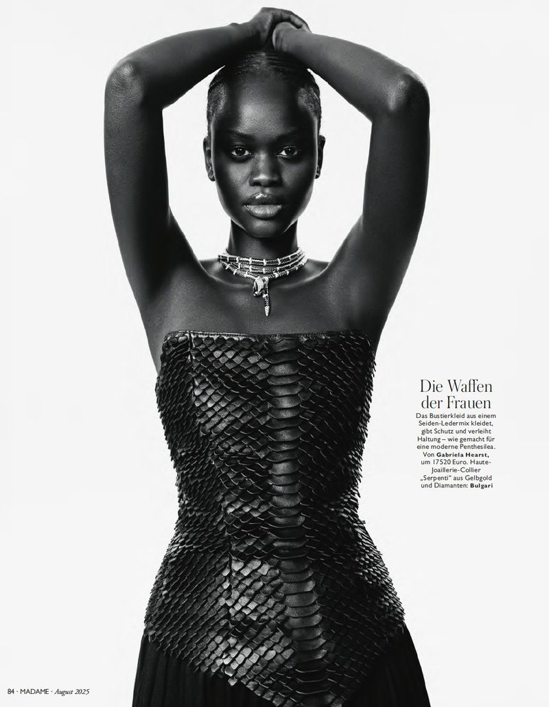 Fashion shot of a black female model in a snakeskin top, silver necklace, and arms overhead, against a white backdrop.