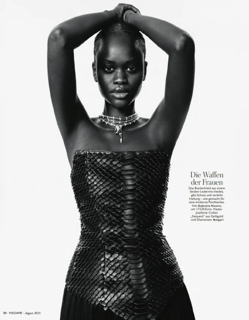 Fashion shot of a black female model in a snakeskin top, silver necklace, and arms overhead, against a white backdrop.