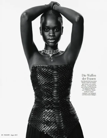 Fashion shot of a black female model in a snakeskin top, silver necklace, and arms overhead, against a white backdrop.
