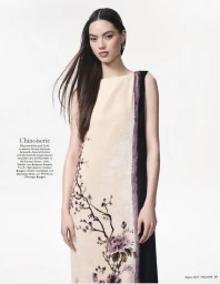 Model in a sleeveless cream chinoiserie dress with purple floral illustration against a plain white studio background.