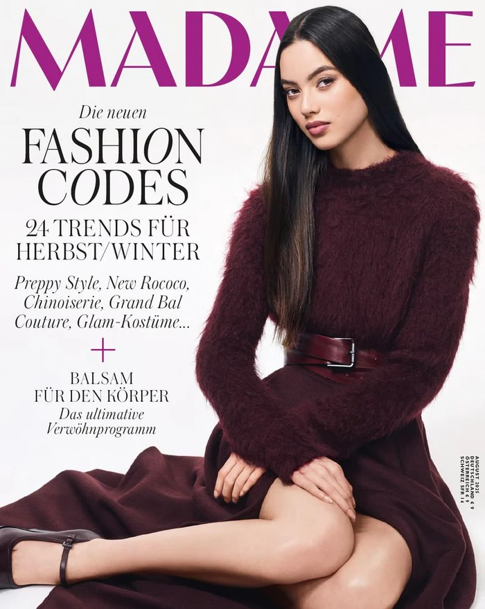 Model with long dark hair wearing a burgundy textured sweater and belted skirt against a seamless white background.