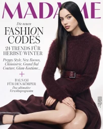 Model with long dark hair wearing a burgundy textured sweater and belted skirt against a seamless white background.