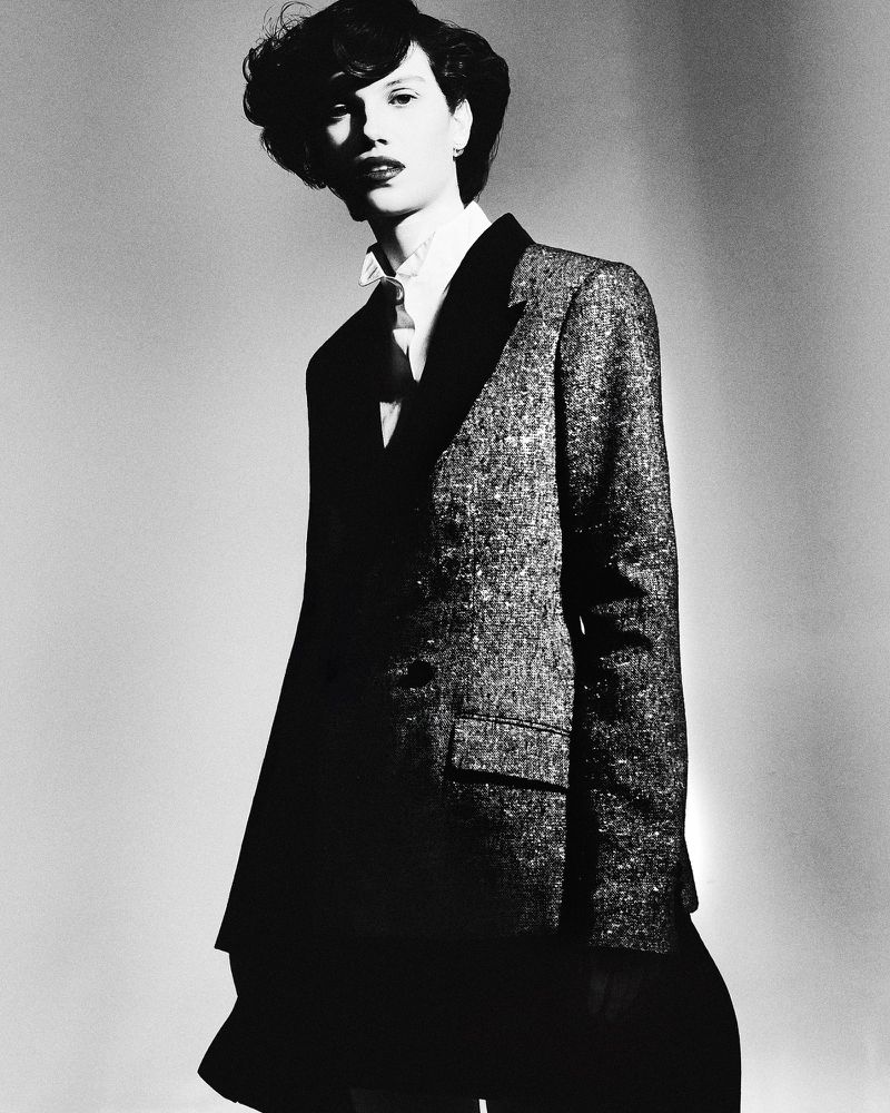 Model with short dark curls wearing a textured tailored blazer with lapels and collared shirt in black and white.