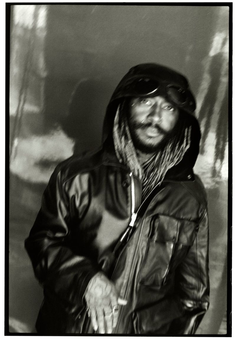 Close-up portrait of Thundercat wearing a black leather hooded jacket and goggles, captured in a moody high-contrast monochrome style.