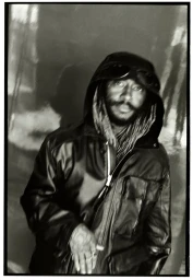 Black and white portrait of musician Thundercat wearing a hooded black leather jacket with built-in goggles.