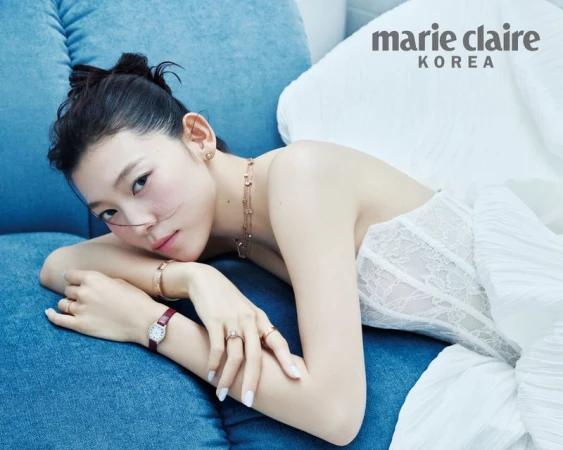 Model Sol Jeong in a white lace bridal corset with luxury jewellery, reclining against a blue textured sofa.