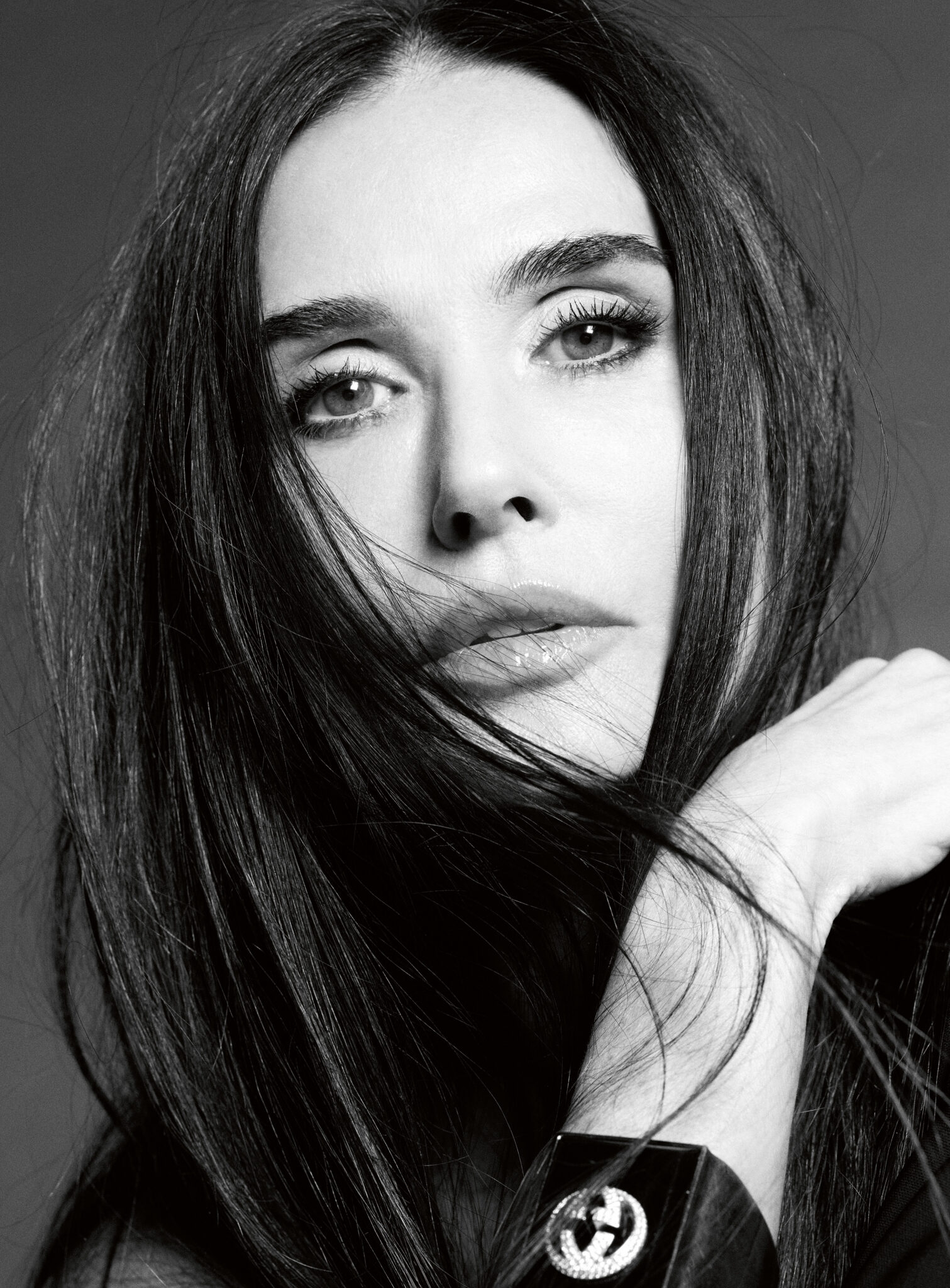 Close-up portrait of Demi Moore wearing a dark cuff bracelet with a prominent circular logo for V Magazine.
