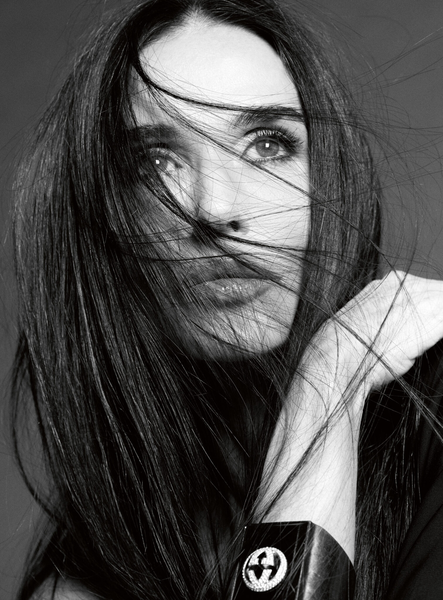 Black and white close up portrait of Demi Moore with windblown dark hair across her face wearing a wide cuff bracelet.
