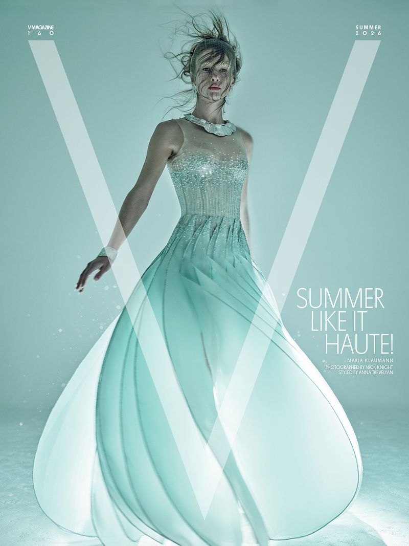Model posing in a sheer, light blue-green embellished gown with flowing skirt against a minimalist, bright aqua studio background.