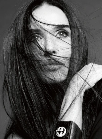 Black and white close up portrait of Demi Moore with windblown dark hair across her face wearing a wide cuff bracelet.