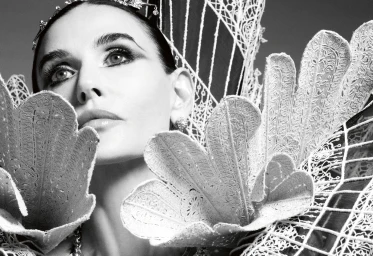 Demi Moore wearing an elaborate sculptural white lace collar and tiara in a black and white fashion portrait.
