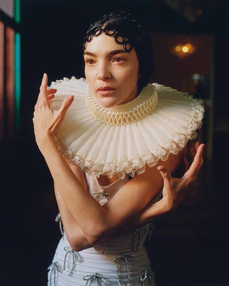 Striking fashion portrait of a woman in a white dress with a ruffled collar, set against a softly lit, dark background, fashion shoot.