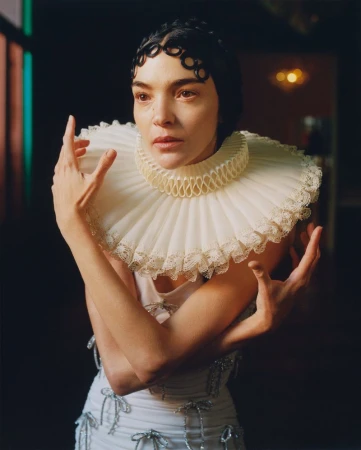 Striking fashion portrait of a woman in a white dress with a ruffled collar, set against a softly lit, dark background, fashion shoot.