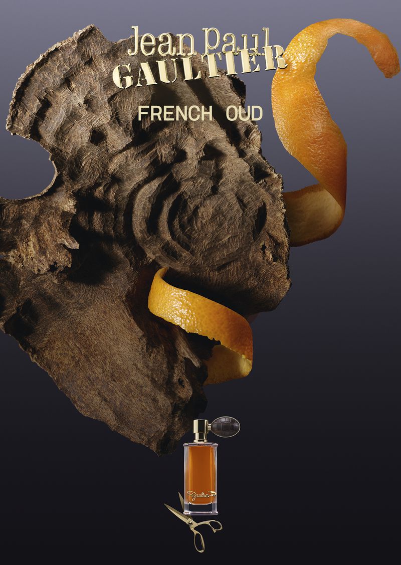 Jean Paul Gaultier French Oud fragrance bottle with golden scissors beneath a carved wood piece wrapped in a spiral orange peel.