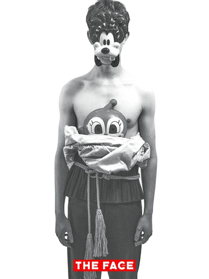 Model wearing a cartoon character face mask, metallic wrapped torso, and tassel rope belt against a white seamless background.
