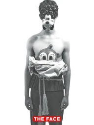 Model wearing a cartoon character face mask, metallic wrapped torso, and tassel rope belt against a white seamless background.