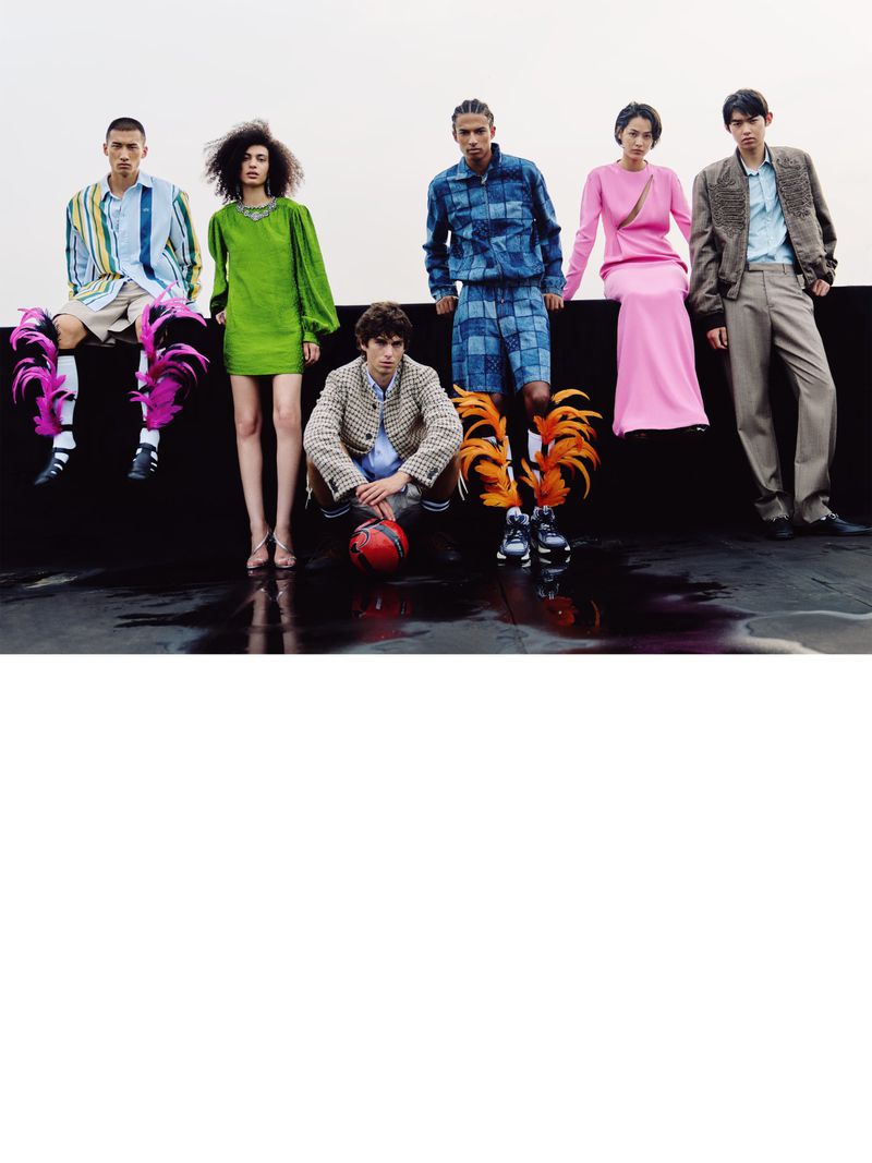Six fashion models posing in colorful designer outfits with feather shoe accents against an overcast sky.