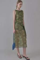 Model wearing a green floral semi-sheer sleeveless midi dress and black kitten heels against a neutral grey studio backdrop.