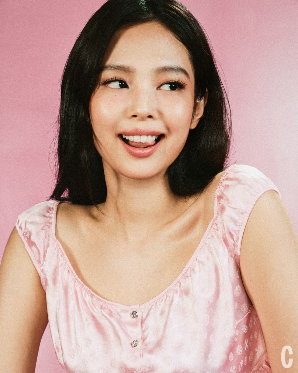 Jennie Kim smiling in a pastel pink satin patterned top against a soft pink backdrop.